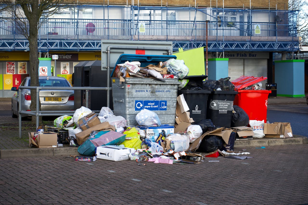 who-we-are An urban scene depicting overflowing bins and garbage in a parking lot, indicating waste management issues.