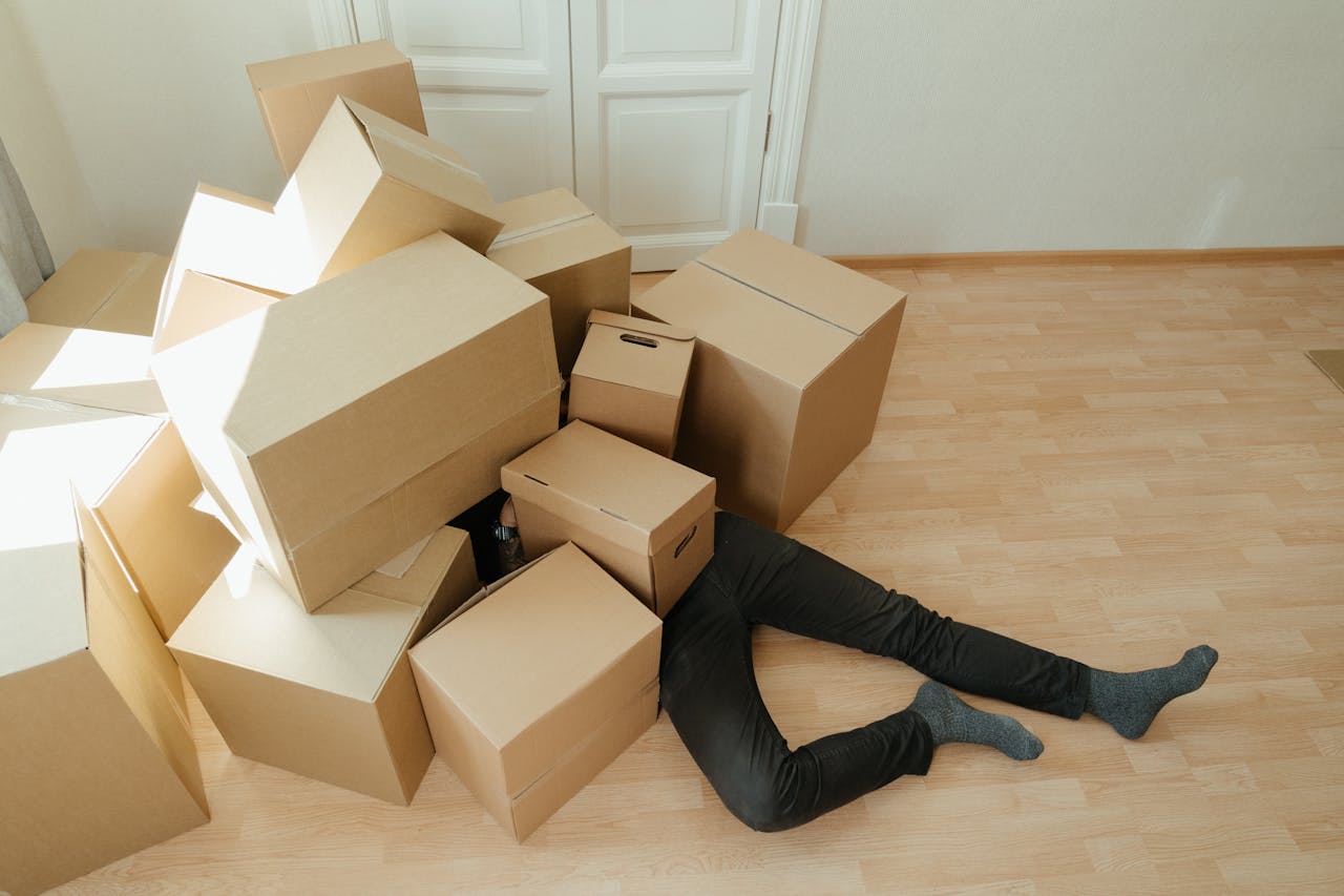 why-choose-us A person overwhelmed by cardboard boxes during a home move, symbolizing stress and relocation.